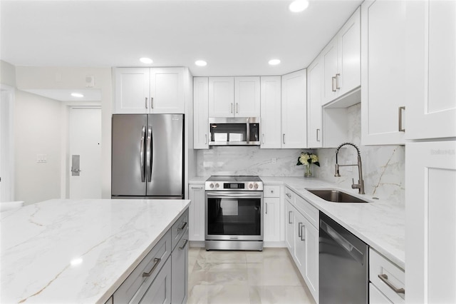 kitchen featuring appliances with stainless steel finishes, a sink, light stone counters, and decorative backsplash