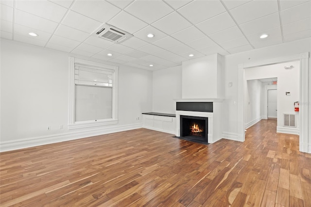 unfurnished living room featuring a fireplace with flush hearth, visible vents, baseboards, and wood finished floors