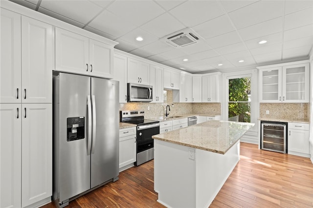 kitchen with white cabinets, wine cooler, glass insert cabinets, light stone counters, and stainless steel appliances