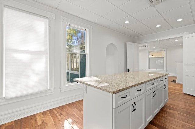 kitchen featuring a paneled ceiling, a kitchen island, wood finished floors, white cabinetry, and light stone countertops