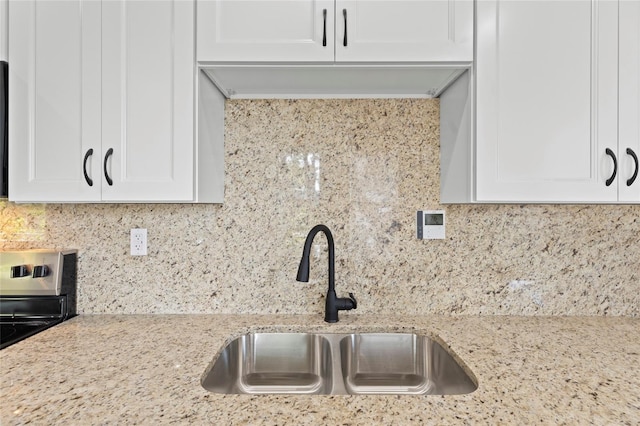 kitchen featuring tasteful backsplash, light stone countertops, stainless steel range with electric cooktop, white cabinetry, and a sink