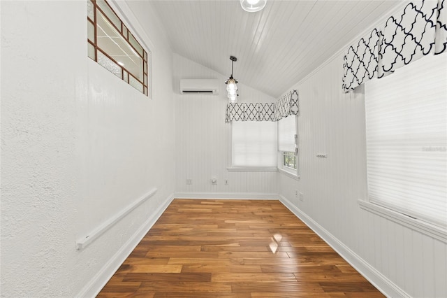 unfurnished dining area with an AC wall unit, vaulted ceiling, baseboards, and wood finished floors