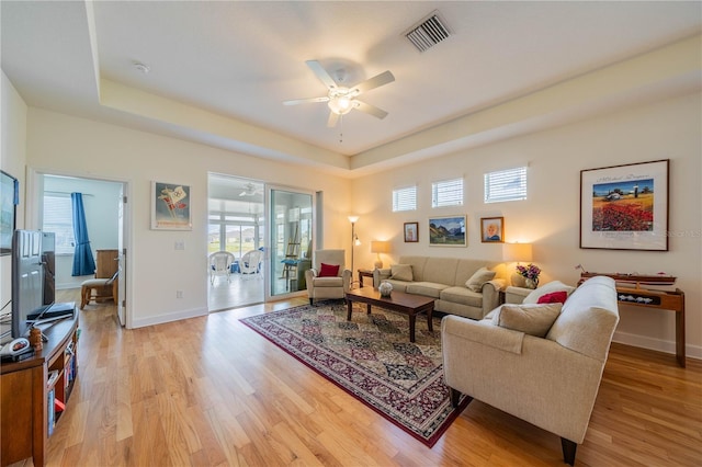 living area featuring light wood-style flooring, visible vents, and a raised ceiling