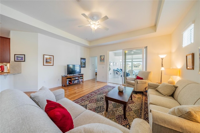 living room featuring ceiling fan, wood finished floors, a raised ceiling, and baseboards