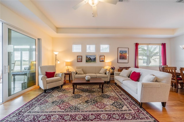 living room featuring a ceiling fan, light wood-type flooring, and a tray ceiling