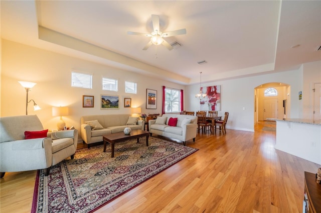 living area with ceiling fan, arched walkways, visible vents, a tray ceiling, and light wood finished floors