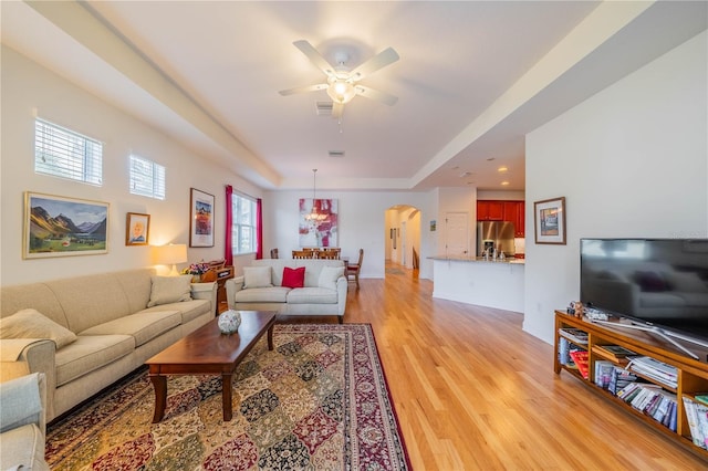 living area featuring arched walkways, plenty of natural light, light wood-style flooring, and ceiling fan