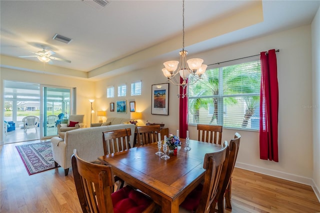 dining space with light wood-style flooring, visible vents, and a tray ceiling