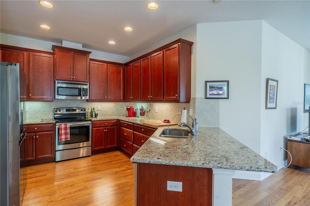 kitchen featuring appliances with stainless steel finishes, a peninsula, light stone countertops, light wood-type flooring, and a sink