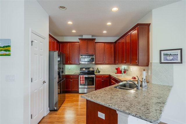 kitchen with a peninsula, a sink, light wood-style floors, appliances with stainless steel finishes, and light stone countertops