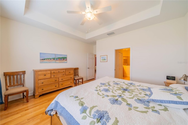 bedroom featuring a raised ceiling, visible vents, ceiling fan, and wood finished floors