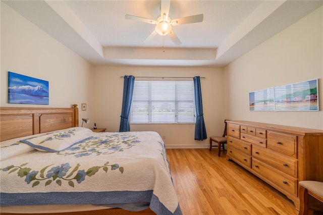 bedroom featuring ceiling fan, light wood-style flooring, baseboards, and a raised ceiling