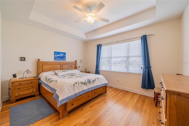 bedroom featuring light wood-style flooring, baseboards, a raised ceiling, and a ceiling fan