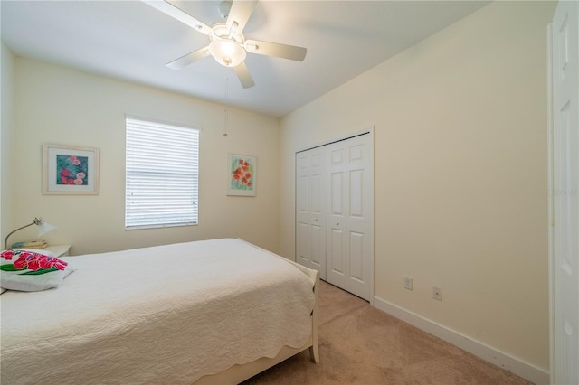 bedroom with baseboards, ceiling fan, a closet, and light colored carpet