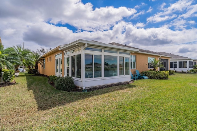 rear view of house featuring a sunroom, a lawn, and stucco siding