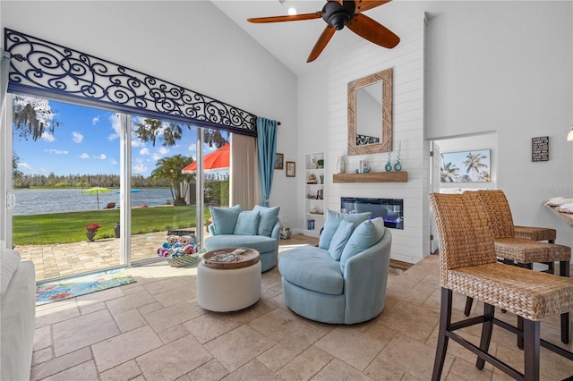 sitting room with high vaulted ceiling, a fireplace, a water view, and stone tile flooring