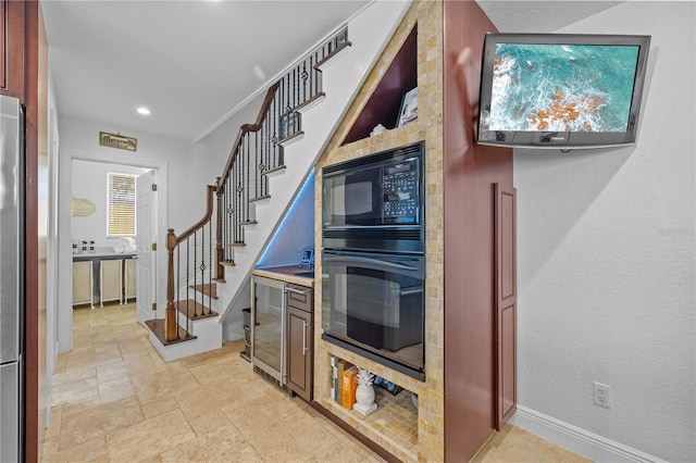 kitchen featuring black appliances, stone tile flooring, recessed lighting, wine cooler, and baseboards