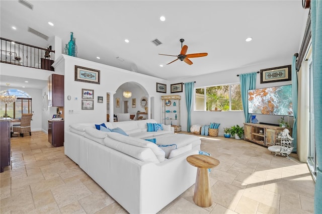 living room with visible vents, stone tile floors, ceiling fan with notable chandelier, recessed lighting, and arched walkways