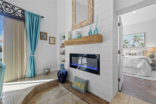 living area with a glass covered fireplace, stone tile floors, built in shelves, and a towering ceiling