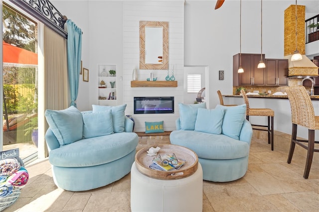 living area featuring a glass covered fireplace, a high ceiling, and stone tile flooring