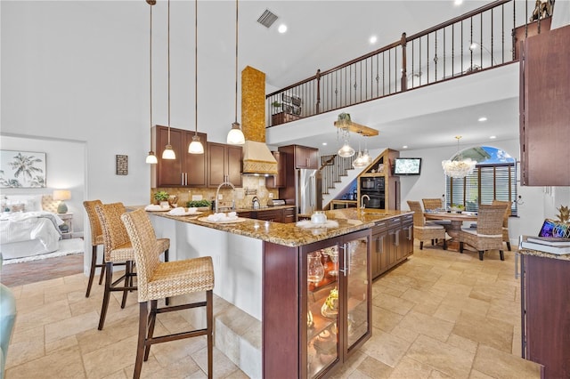 kitchen with visible vents, custom range hood, stone tile floors, decorative backsplash, and stainless steel fridge