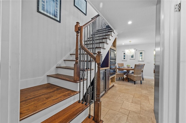 staircase with stone tile flooring, a notable chandelier, recessed lighting, and baseboards