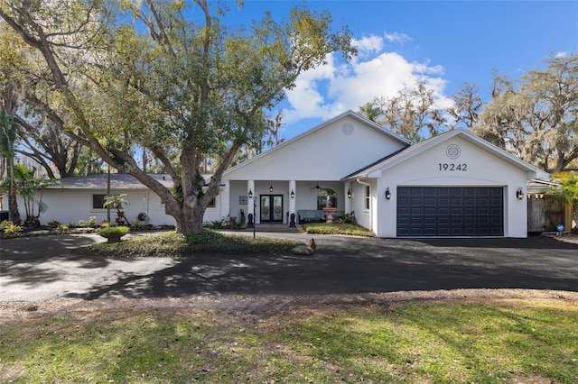 view of front of house with stucco siding, french doors, an attached garage, and driveway