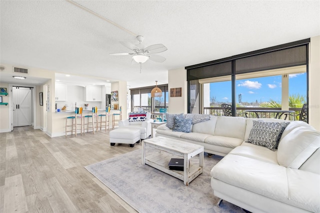 living area with a textured ceiling, ceiling fan, light wood-style flooring, and visible vents