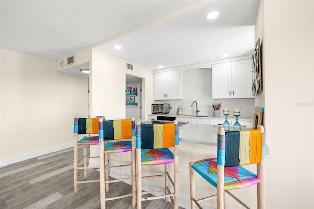 kitchen with light countertops, white cabinets, a sink, light wood-type flooring, and baseboards