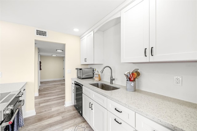 kitchen with stainless steel range, white cabinetry, a sink, and light stone countertops