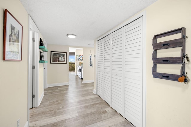 hall with light wood-style flooring, baseboards, and a textured ceiling