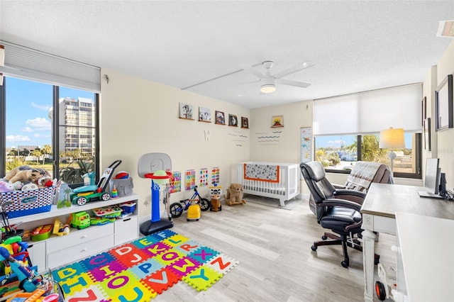 game room with a view of city, a textured ceiling, light wood-style flooring, and a healthy amount of sunlight