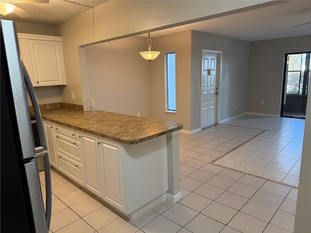 kitchen featuring decorative light fixtures, light tile patterned floors, freestanding refrigerator, white cabinets, and a peninsula