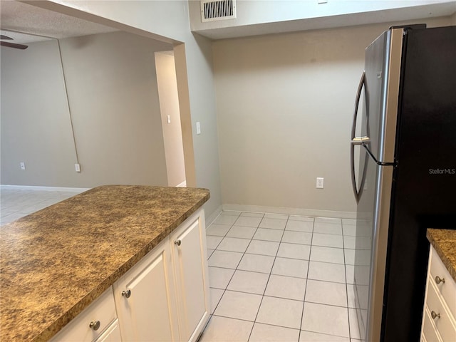 kitchen featuring visible vents, freestanding refrigerator, light tile patterned flooring, white cabinetry, and dark stone countertops