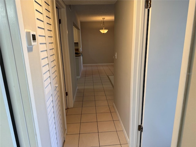 hallway with light tile patterned flooring, a textured ceiling, and baseboards