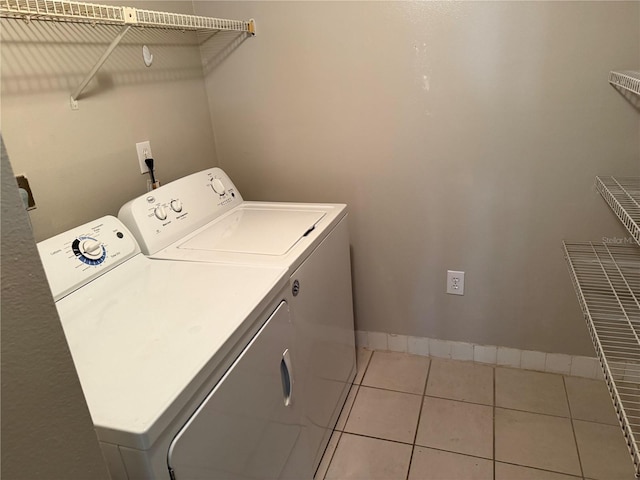 clothes washing area with light tile patterned floors, laundry area, baseboards, and washer and dryer