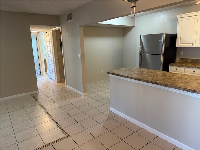 kitchen featuring light tile patterned flooring, visible vents, white cabinetry, freestanding refrigerator, and dark countertops