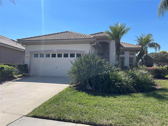 view of front of property featuring an attached garage, a tile roof, concrete driveway, stucco siding, and a front lawn