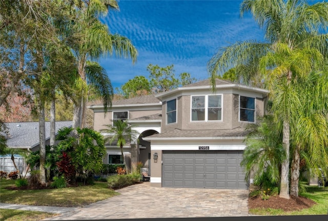 traditional-style house with a garage, decorative driveway, and stucco siding