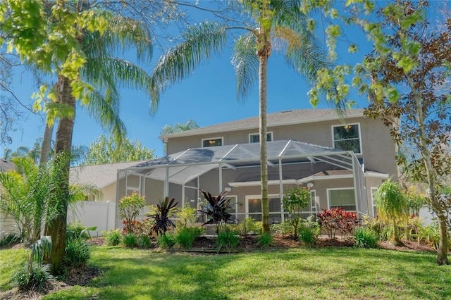 rear view of property featuring a lanai, stucco siding, a lawn, and fence