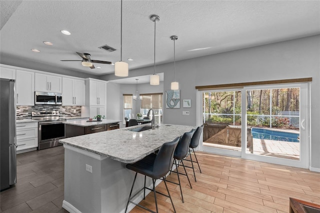 kitchen featuring visible vents, an island with sink, stainless steel appliances, light wood-type flooring, and a sink