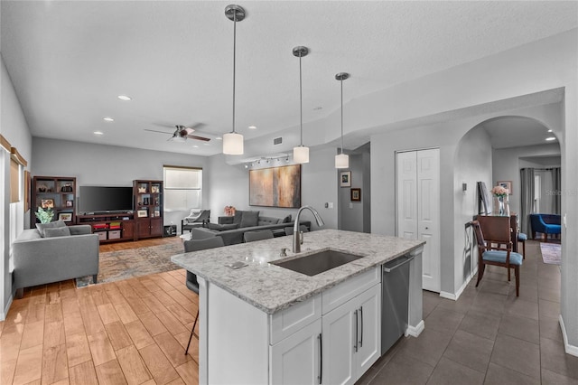 kitchen with arched walkways, hanging light fixtures, white cabinetry, a sink, and dishwasher