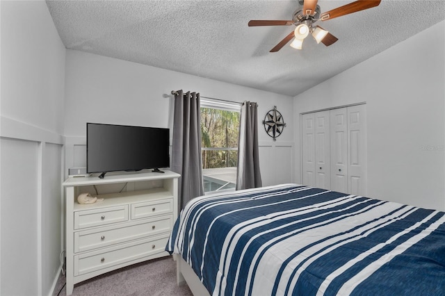 bedroom with a textured ceiling, a ceiling fan, vaulted ceiling, a closet, and dark colored carpet