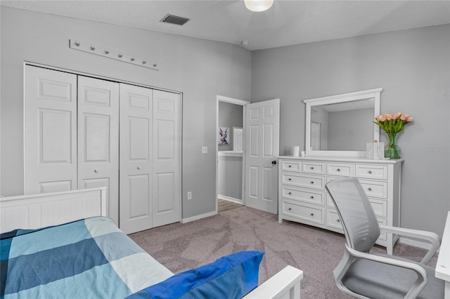 bedroom with a closet, visible vents, light carpet, and a textured ceiling