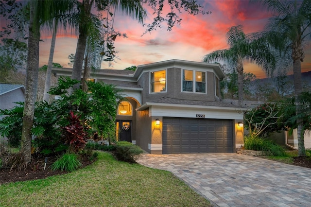 view of front of house with a yard, decorative driveway, an attached garage, and stucco siding