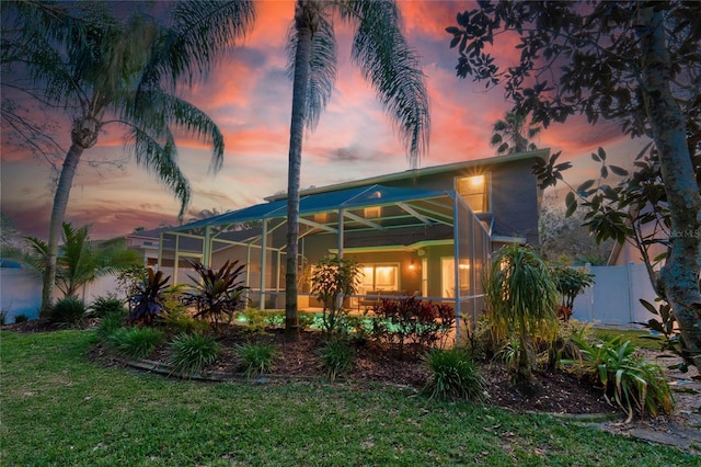 back of property at dusk featuring glass enclosure, a yard, and fence