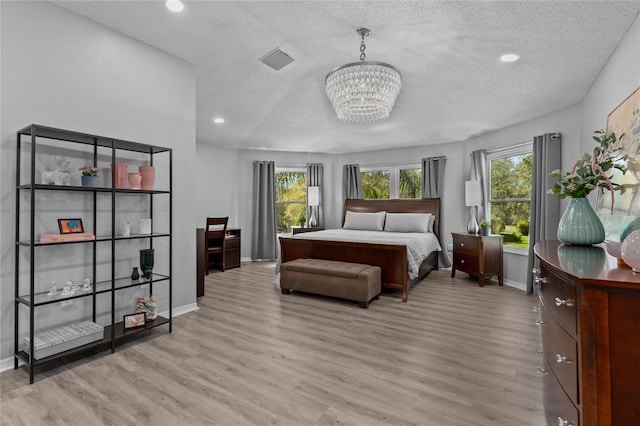 bedroom featuring visible vents, an inviting chandelier, light wood-style floors, a textured ceiling, and baseboards