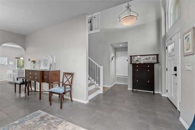 foyer entrance featuring baseboards, arched walkways, a towering ceiling, tile patterned flooring, and stairs