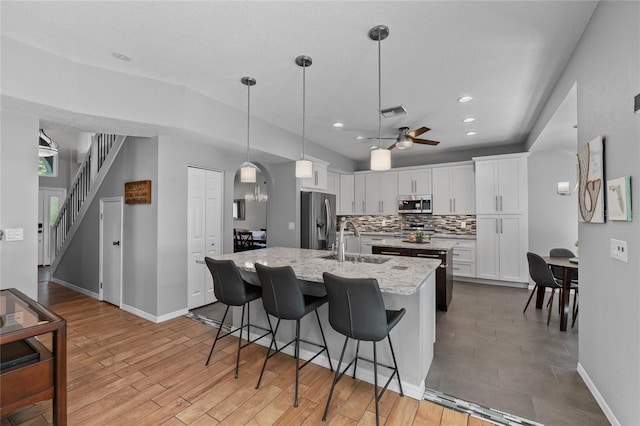 kitchen featuring a sink, white cabinetry, appliances with stainless steel finishes, decorative backsplash, and an island with sink