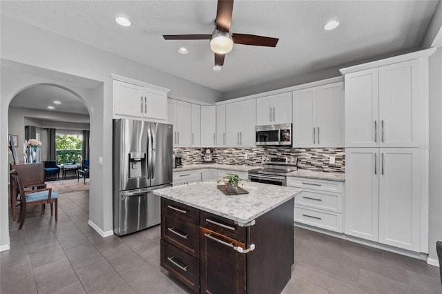 kitchen featuring arched walkways, white cabinets, a center island, stainless steel appliances, and backsplash